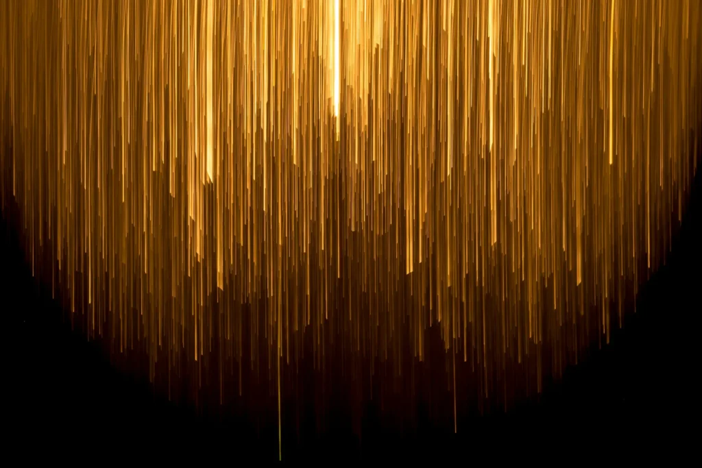 Luces verticales doradas descendiendo en un patrón abstracto sobre fondo negro, simbolizando la innovación y creatividad en el diseño de experiencia de usuario.