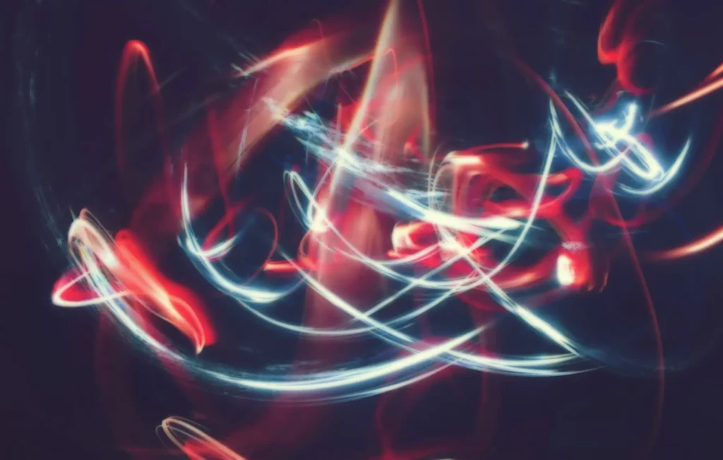 Trazos abstractos de luz en tonos rojos, blancos y azules sobre fondo oscuro, representando la energía y dinamismo del diseño web.